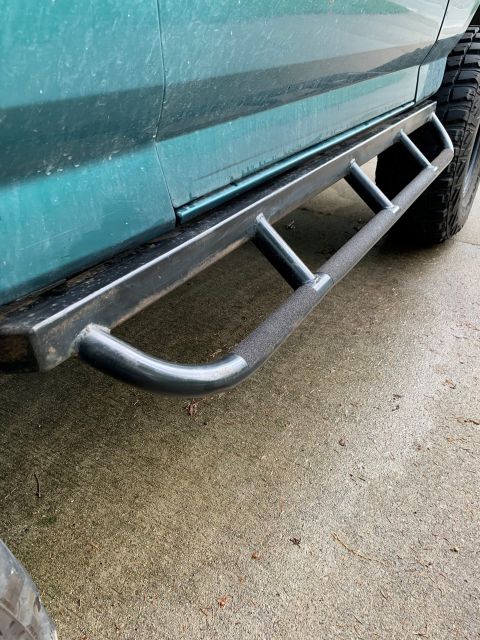 1996 Ford Bronco - Custom rock sliders are attached to the side of a green SUV, with a portion of a tire visible.