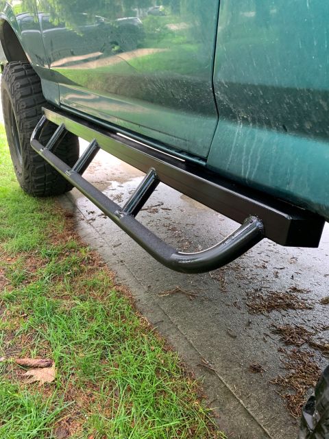 1996 Ford Bronco - Side view of a green SUV aftermarket black tubular rock sliders and off-road tires.