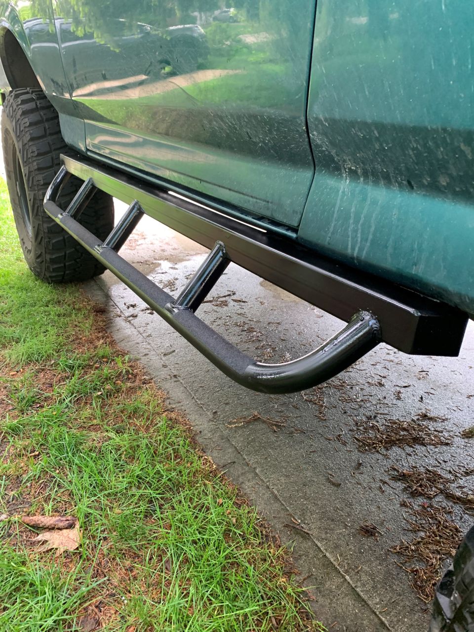 Green SUV side with black tubular rock sliders and large tires