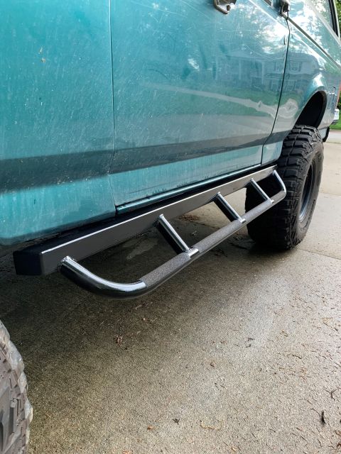 1996 Ford Bronco - Aftermarket step bars installed on a 1996 Ford Bronco, with large off-road tires visible.