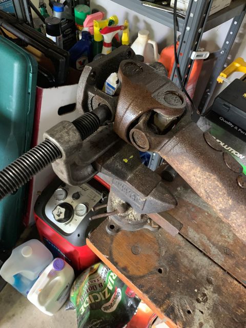 1996 Ford Bronco - A rusty driveshaft component is secured in a vise, surrounded by various workshop items.