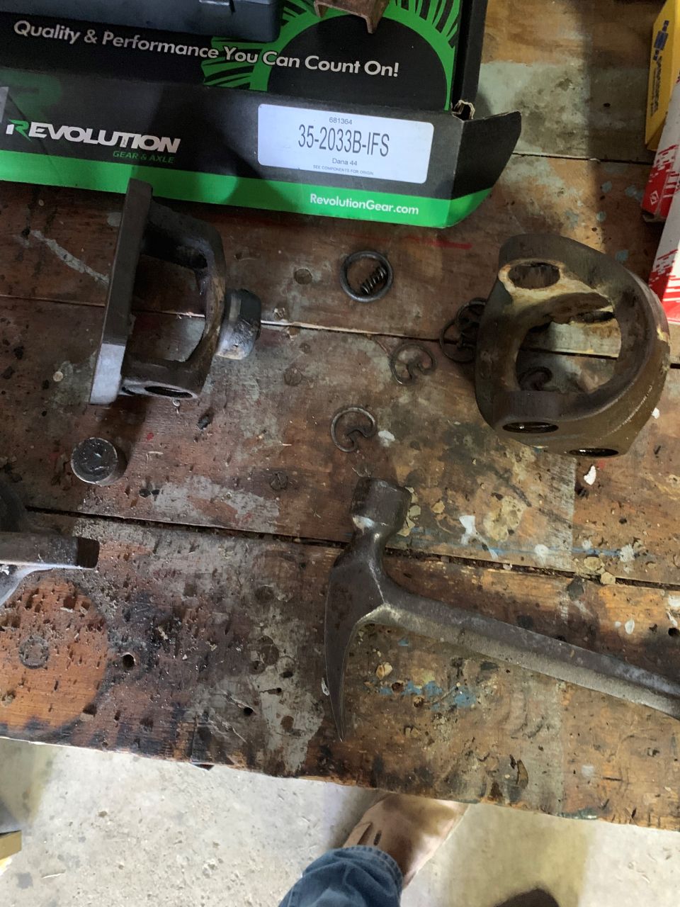 Disassembled metal parts and a hammer on a wooden workbench; a box labeled 'Revolution Gear' is in the background
