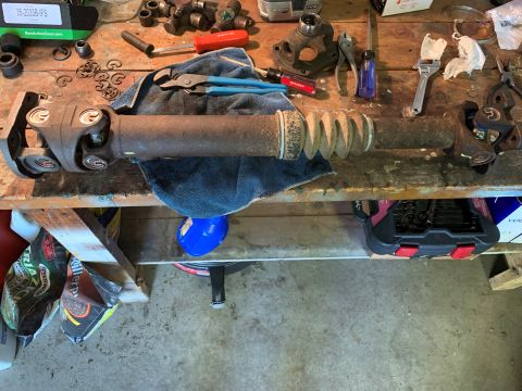 1996 Ford Bronco - A driveshaft, likely for a truck or SUV, rests on a workbench alongside various tools and spare parts.
