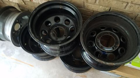 1994 Ford Bronco - A collection of black steel wheels is shown, some with visible lug nut holes and center caps.