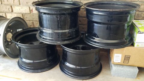 1994 Ford Bronco - A collection of four black steel wheels and one silver alloy wheel are displayed outdoors.