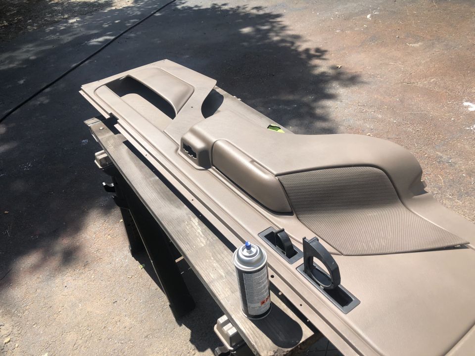 Tan car door panel with black handles and a spray can on a wooden surface