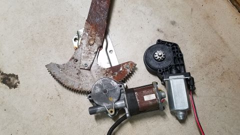 1994 Ford Bronco - Two window motors and a manual window regulator mechanism are laid out on a concrete surface.