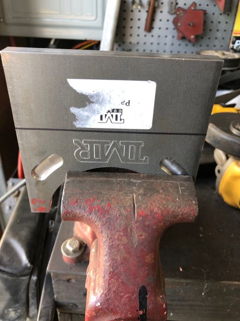 1992 Jeep Wrangler - Metal part with 'TMIR' logo held in a vise, likely in a workshop setting.