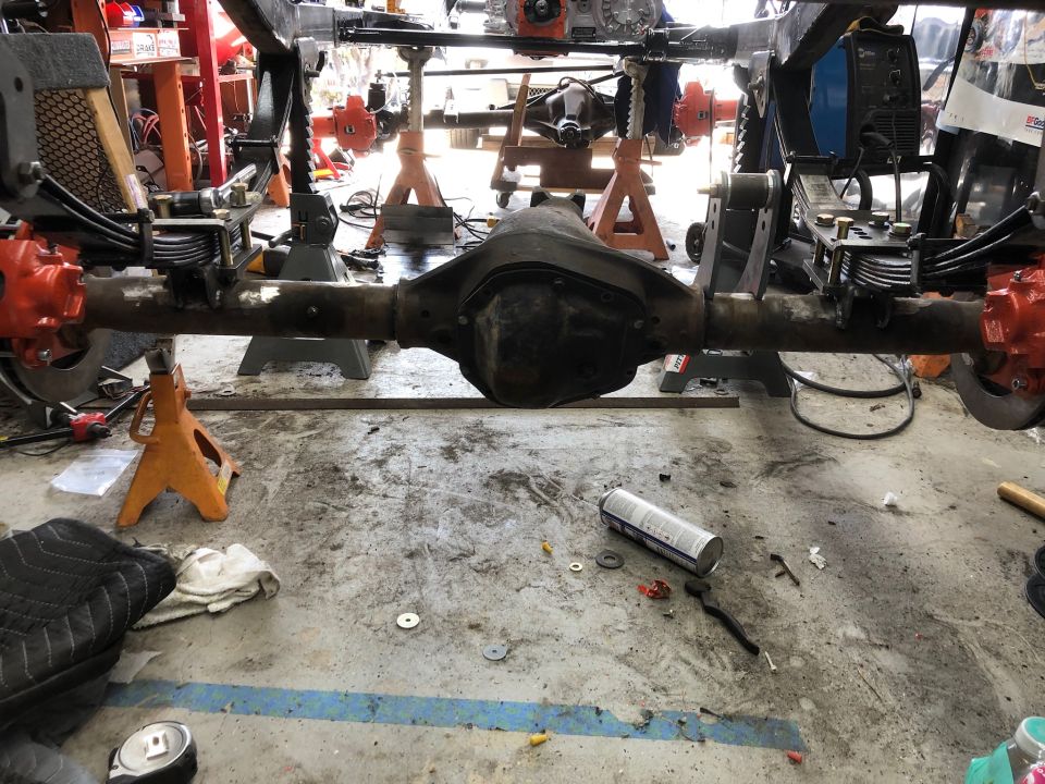 vehicle's rear axle assembly on jack stands in a garage, with tools and parts scattered around