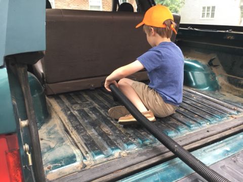 1996 Ford Bronco - A young boy cleans out the dusty bed of a pickup truck with a vacuum hose.