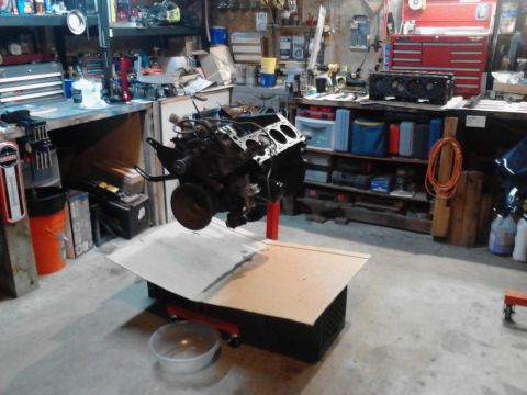 1978 Ford Bronco - An engine is mounted on an engine stand in a cluttered garage setting.