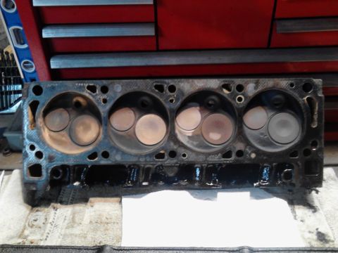 1978 Ford Bronco - Engine cylinder head removed from a vehicle, resting on a workbench.