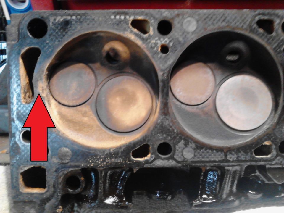 Close-up of an engine cylinder head with valves visible. A red arrow points to a damaged area
