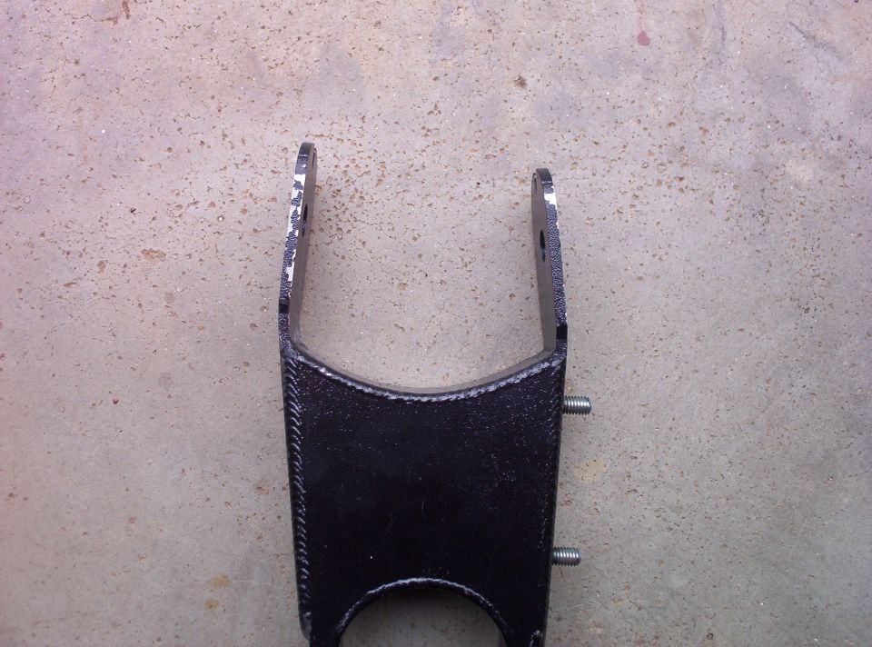 Black metal automotive part with two bolts and chipped paint on a concrete surface