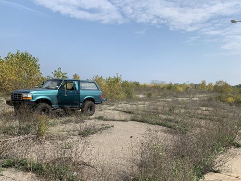 1996 Ford Bronco - A green 1996 Ford Bronco is parked in a dry, grassy area under a partly cloudy sky.