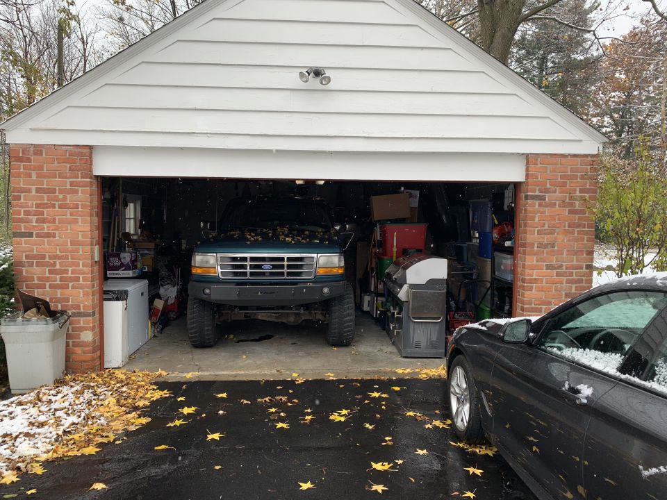 Green Ford truck parked in a garage, with a black car partially visible on the right