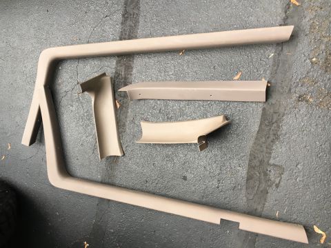 1996 Ford Bronco - Several tan interior trim pieces are laid out on a dark, wet asphalt surface.