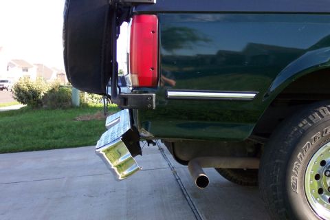 1992 Ford Bronco - Close-up of the rear driver-side corner of a dark green Ford Bronco showing a bent and torn chrome rear bumper end pulled away from the bod…