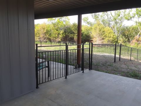 1994 Ford Bronco - A concrete patio area is enclosed by a black metal fence and gate, with trees visible beyond.