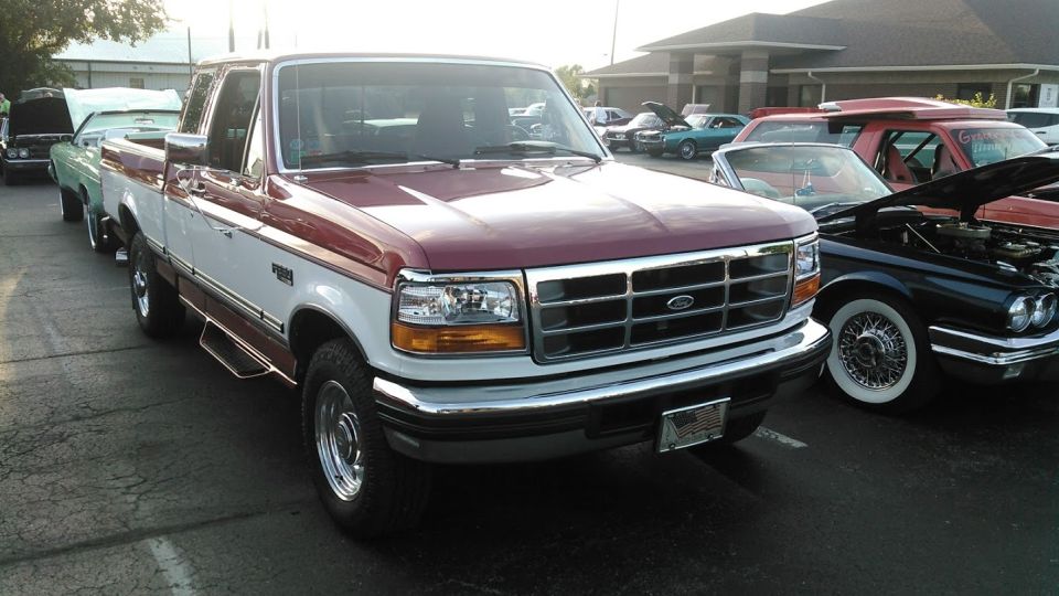 Maroon and white Ford F-250 truck, front 3/4 view, parked in a lot with other vehicles