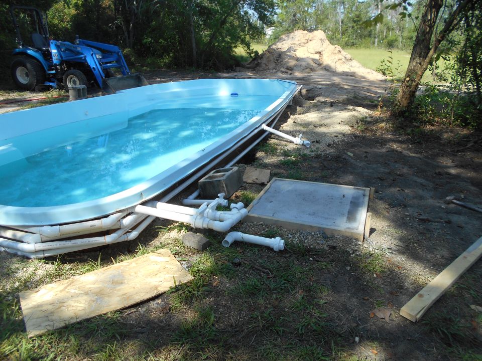 In-ground swimming pool installation with plumbing and a blue tractor in the background