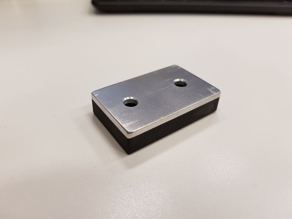 Rectangular metal and rubber part with two holes on a light-colored surface