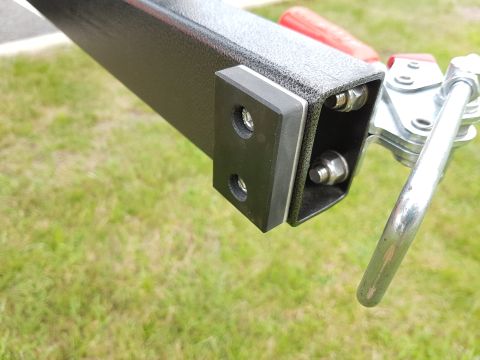 1978 Ford Bronco - Detail of a metal bracket assembly with visible bolts and a lever mechanism, set against a grassy background.