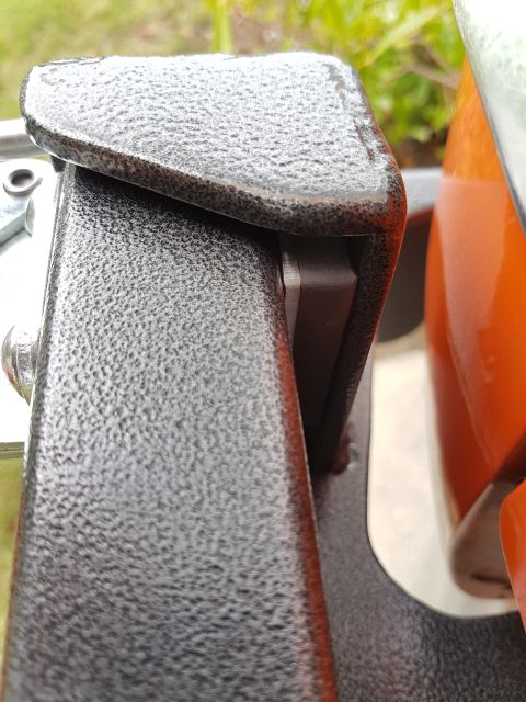 1978 Ford Bronco - A textured metal bracket is shown in close-up, with an orange object partially visible to the right.