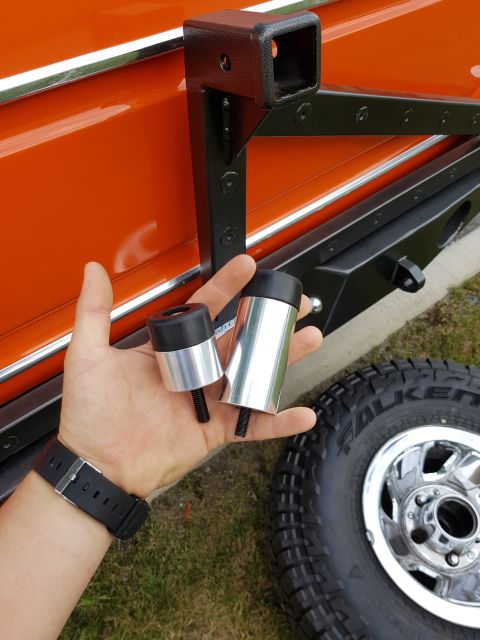 1978 Ford Bronco - A hand holds two aluminum door bump stops next to the rear of an orange 1978 Ford Bronco, with a spare tire and wheel visible.