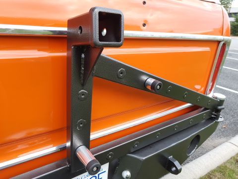 1978 Ford Bronco - Close-up of an orange vehicle's rear, a black spare tire carrier and hitch receiver assembly.