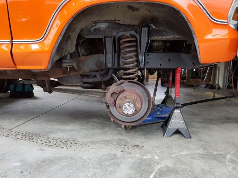 1978 Ford Bronco - Front passenger side suspension and brake assembly of an orange vehicle being worked on.