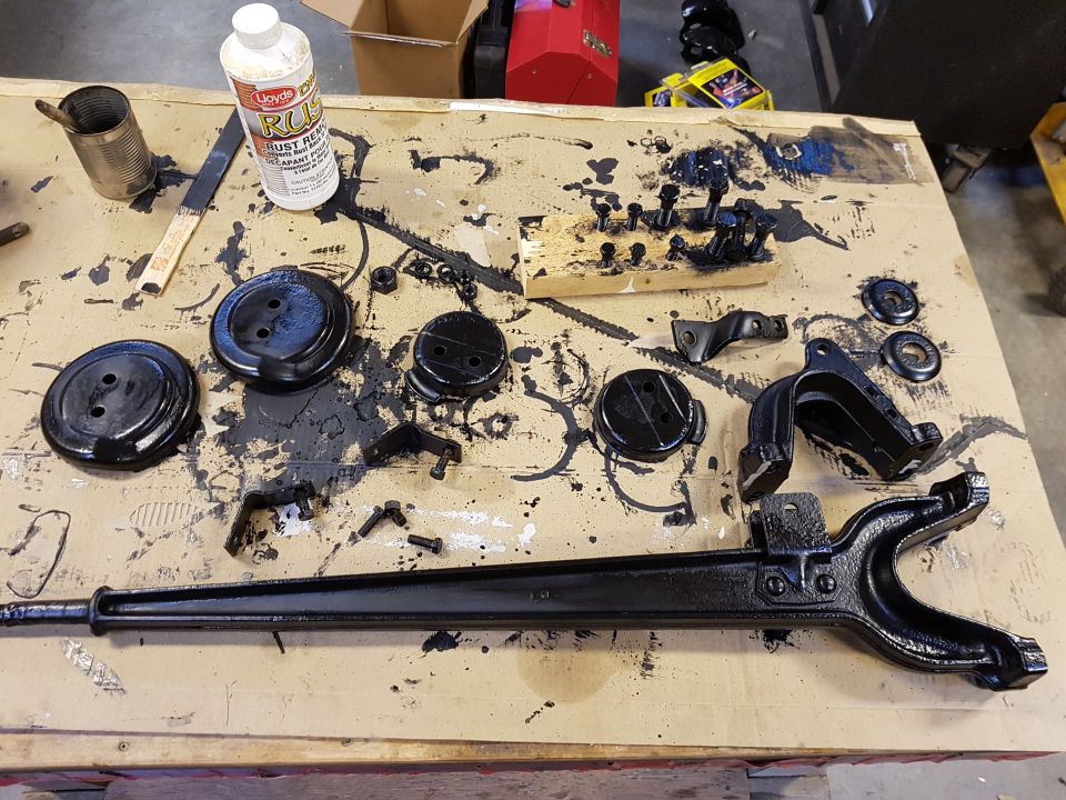 various black painted car parts and a bottle of rust remover on a messy workbench
