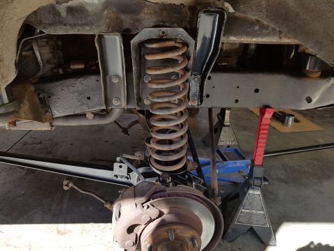 1978 Ford Bronco - Close-up view of vehicle suspension components, including a coil spring and brake assembly, supported by jack stands.