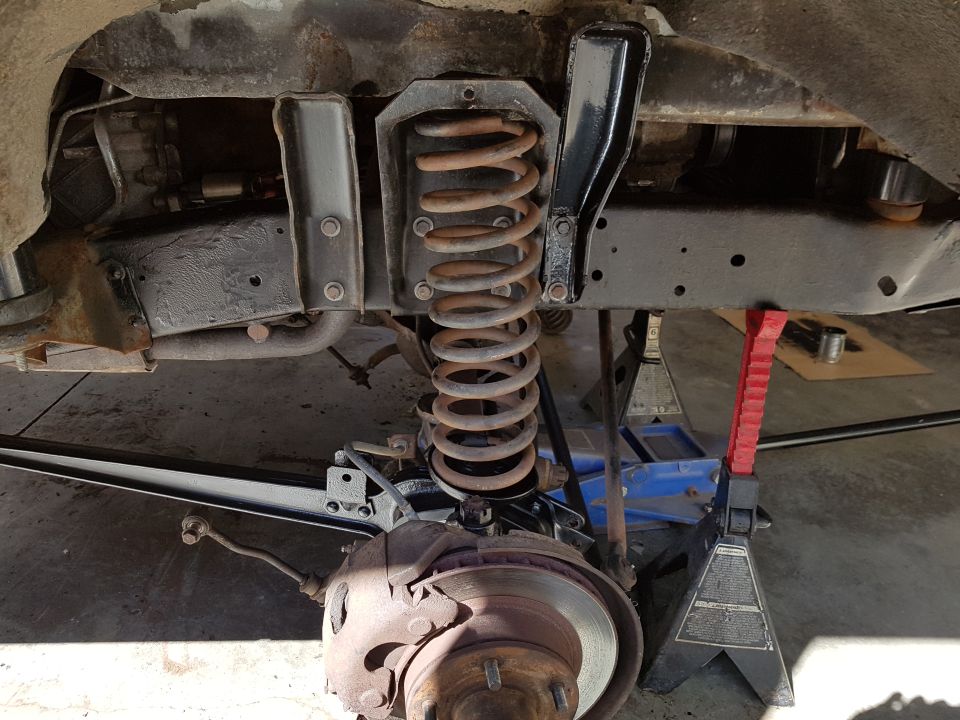 Vehicle suspension with coil spring, brake rotor, and jack stands. Rusty metal parts visible