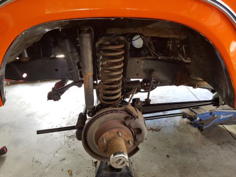 1978 Ford Bronco - Close-up view of the front suspension and wheel assembly of an orange vehicle, showing the coil spring and shock absorber.