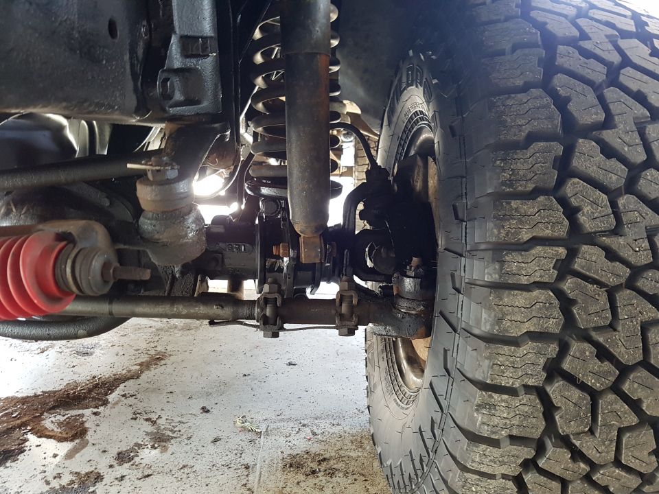 Tire and suspension components of a vehicle, showing a large off-road tire, coil spring, shock absorber, and steering linkage