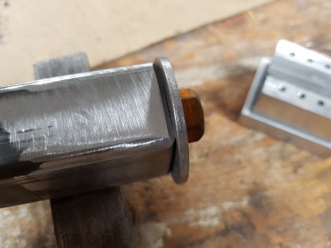 1978 Ford Bronco - Close-up of a metal bracket and bolt, with another component in the background on a wooden surface.