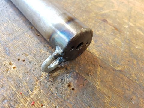 1978 Ford Bronco - A metal tube with a welded eyelet and multiple holes is shown on a workbench.