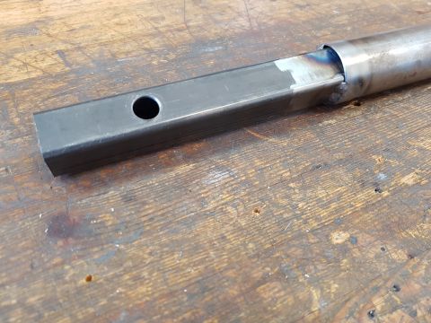 1978 Ford Bronco - A metal tube with a hole is welded to another metal tube, resting on a wooden surface.