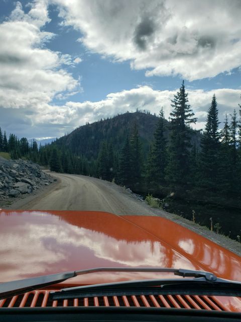 1978 Ford Bronco - Driving on a dirt road through a mountainous, forested area, with the hood and windshield wipers of an orange vehicle visible in the foregr…