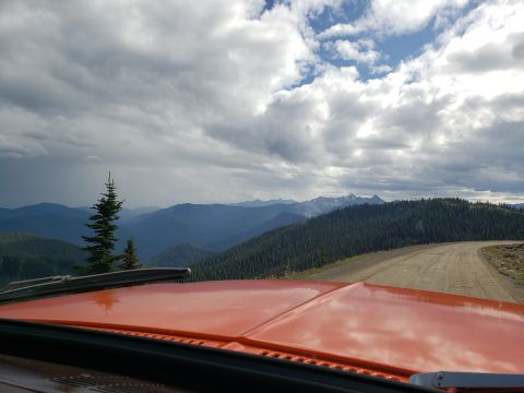 1978 Ford Bronco - View from inside a vehicle driving on a dirt road through a mountainous, forested area under a cloudy sky.