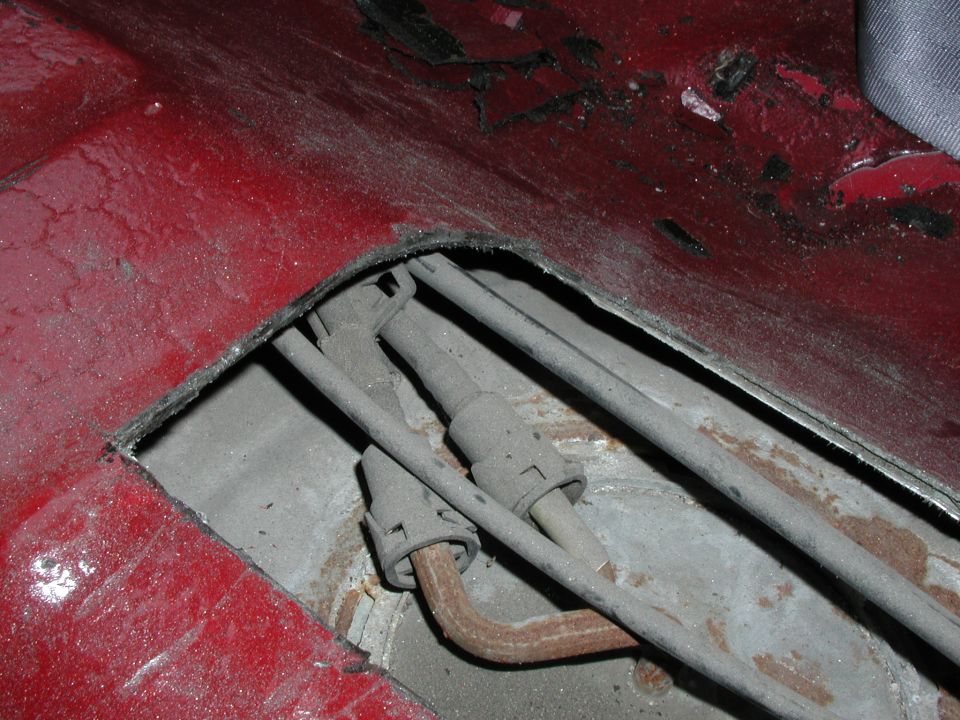 Cutaway opening in red floor pan exposing rusty fuel and brake lines underneath