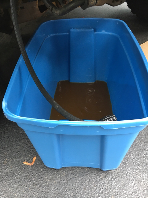 1996 Ford Bronco - Fluid is being drained into a blue tub from a hose connected to a vehicle's undercarriage.