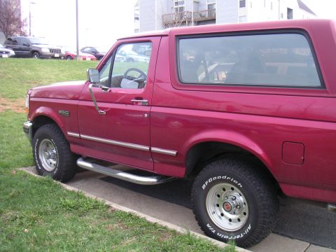 1994 Ford Bronco - A red Ford Bronco is seen from the side, parked next to a grassy area.