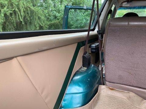 1996 Ford Bronco - The interior of a green SUV is visible, tan upholstery and a teal spare tire cover.