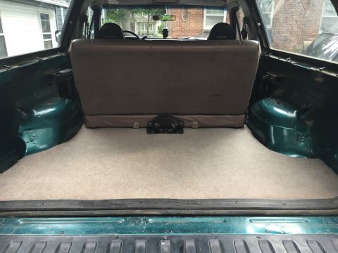 1996 Ford Bronco - The interior cargo space of a green SUV is shown, a carpeted floor and folded rear seats.