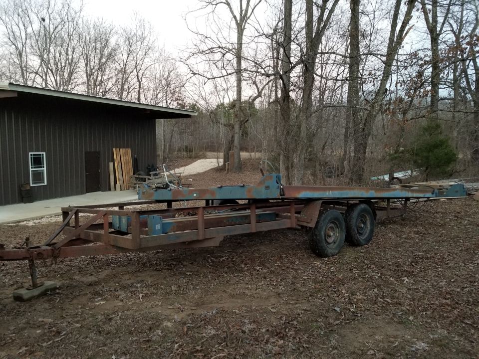 rusted car hauler trailer with dual axles parked on dirt in front of a metal building