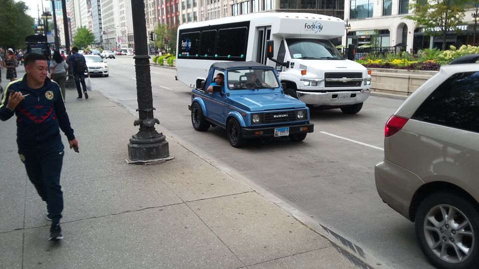 Blue Suzuki Samurai with black wheels and a black soft top drives on a city street