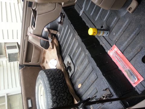 1995 Ford Bronco - The cargo area of a vehicle contains a spare tire, a can of spray, and a set of cleaning brushes.