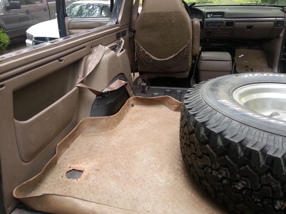 Interior of a Ford Bronco showing a spare tire, tan floor mat, and dashboard.